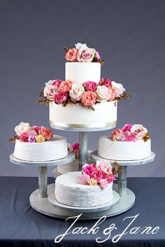 three tiered wedding cake with pink and white flowers on each layer, sitting on a silver stand