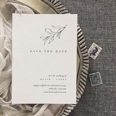 a wedding save the date card on top of a silver plate with postage and feathers