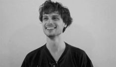 a black and white photo of a young man with curly hair smiling at the camera