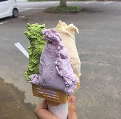 a person holding up an ice cream cone with green and purple toppings