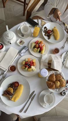 a white table topped with plates and bowls filled with breakfast foods on top of it