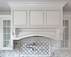 a kitchen with white cabinets and marble counter tops, along with an oven hood over the range