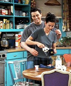 a man and woman standing in a kitchen next to a table