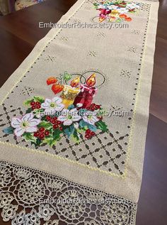 an embroidered table runner with flowers and candles on the edge is sitting on a wooden table