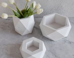 three white vases with flowers in them on a marble countertop next to a wall