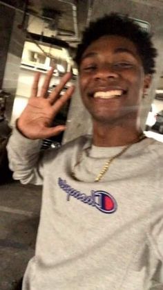 a young man making the peace sign with his hand and smiling at the camera while wearing a champion shirt