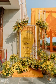 an outdoor ceremony with yellow flowers and orange draping on the side of the building