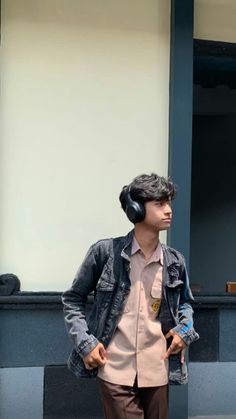 a young man with headphones standing on the side walk in front of a building