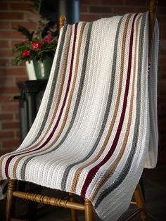 a white blanket sitting on top of a wooden chair next to a potted plant