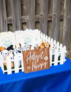 there is a sign that says adopt a puppy next to some stuffed animals on a blue table cloth