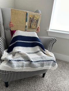 a child is sitting in a chair with a blanket on it and holding up a book