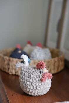 two crocheted chickens sitting on top of a wooden table next to a basket