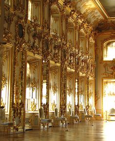 an ornately decorated room with gold trimmings and mirrors on the walls, along with chairs