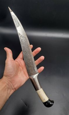 a hand holding a large knife with an intricate design on it's blade and handle