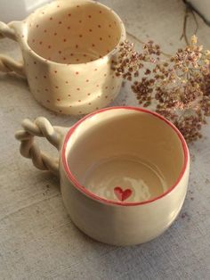 two ceramic bowls with handles are sitting on a table