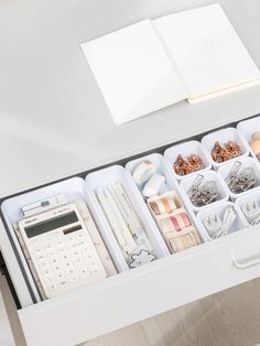 an open drawer with various items in it and a book on the table next to it