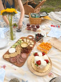 a woman sitting at a picnic table with food on it and flowers in the background