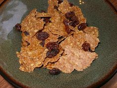 a green plate topped with granola and raisins on top of a wooden table