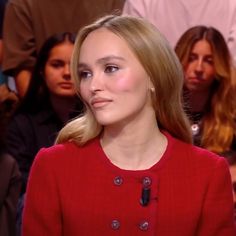 a woman in a red jacket is looking at the camera and people are sitting behind her