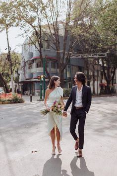 a man and woman holding hands walking down the street with trees in the back ground