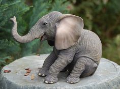 an elephant figurine sitting on top of a stone slab in front of trees