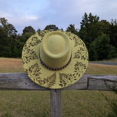 This hand burnt faux suede wide brim boater hat makes a perfect addition to any nature lover's wardrobe. The earthen chartreuse green material burns a gorgeous deep green allowing the design to stand out. Whimsical ferns, that appear to be blowing in the breeze, are intricately burned by hand using a pyrography machine around the entire crown of the hat. The design is original and completely free-handed. For a finishing touch the hat is adorned with a wooden beaded tie-back hat band. Hat Materia Bohemian Boater Hat With Flat Brim For Garden Party, Bohemian Hats With Flat Crown For Spring, Bohemian Flat Crown Hats For Spring, Bohemian Boater Hat With Curved Brim For Garden Party, Bohemian Boater Hat For Garden Party With Curved Brim, Bohemian Boater Hat With Short Brim For Garden Party, Bohemian Boater Hat For Garden Party With Short Brim, Bohemian Boater Hat For Garden Party, Bohemian Boater Hat With Curved Brim For Country Events