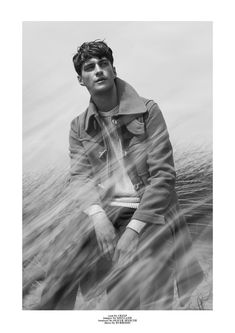 a young man sitting on top of a beach next to the ocean with his hands in his pockets