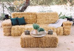 a couch made out of hay sitting on top of a field next to a tree