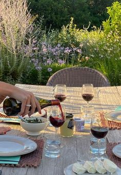 a person pouring wine into a bowl on top of a table with plates and glasses