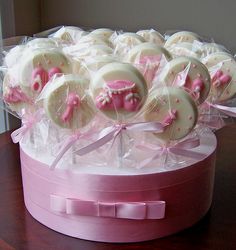 a pink box filled with lots of white and pink candy lollipops on top of a wooden table