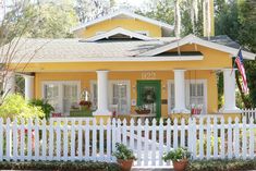 a yellow house with white picket fence and potted plants