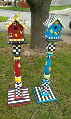 two colorful birdhouses are standing in the grass near a tree and street light pole