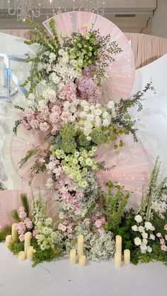 an arrangement of flowers and greenery on display in front of a wall with candles