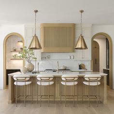 a large kitchen with an island and bar stools in the center, along with two gold pendant lights hanging from the ceiling