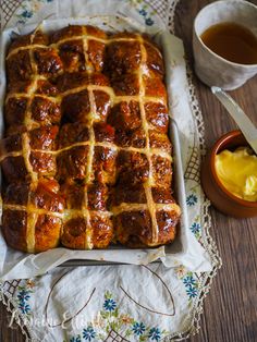 hot cross buns in a baking pan with butter and syrup on the table next to it