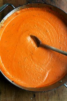 a wooden table topped with a metal pan filled with orange sauce and a spatula