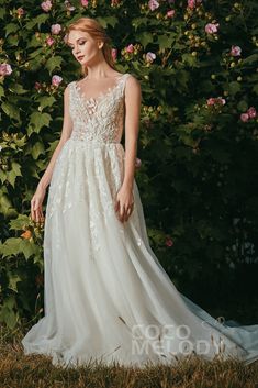 a woman standing in front of a bush wearing a wedding dress with flowers on it