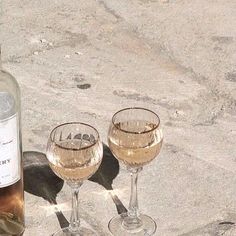 two wine glasses sitting next to a bottle of wine on top of a cement surface