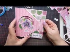 someone is making a card with pink and green designs on the front, while another person's hands are holding it