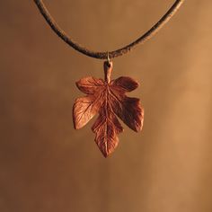 an oak leaf is hanging from a leather cord on a necklace with a metal chain