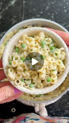 a person holding a small bowl filled with noodles and peas in it's left hand