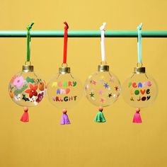 three glass ornaments hanging from a line on a yellow background with colorful tassels