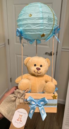 a brown teddy bear sitting in a box with a blue balloon on it's head