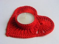 a red knitted candle holder with a white lit candle in the shape of a heart