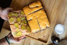 a person holding a piece of cake on top of a wooden cutting board