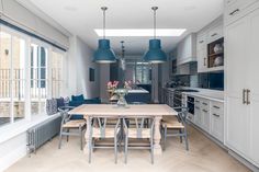 an open kitchen and dining room area with blue pendant lights hanging over the countertop