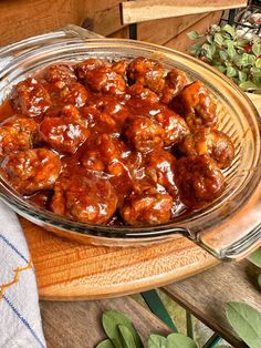 a glass dish filled with meatballs on top of a wooden table next to plants