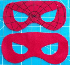 two pieces of red felt are laid out on a cutting board, one has a mask and the other has a spiderman's web