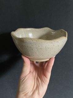 a hand holding a white ceramic bowl with speckles