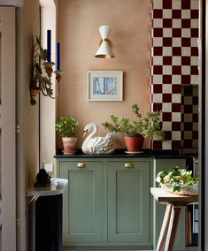 a kitchen with green cabinets and white swans on the counter top in front of potted plants